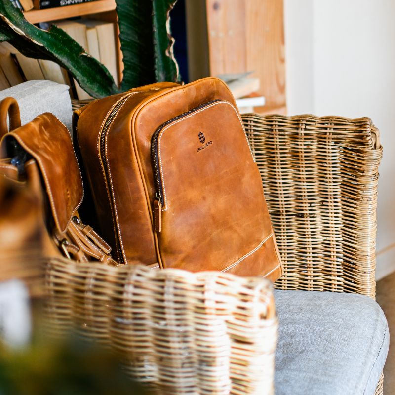 Brown leather bags on a chair with a wicker basket and plant in the background