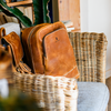 Brown leather bags on a chair with a wicker basket and plant in the background