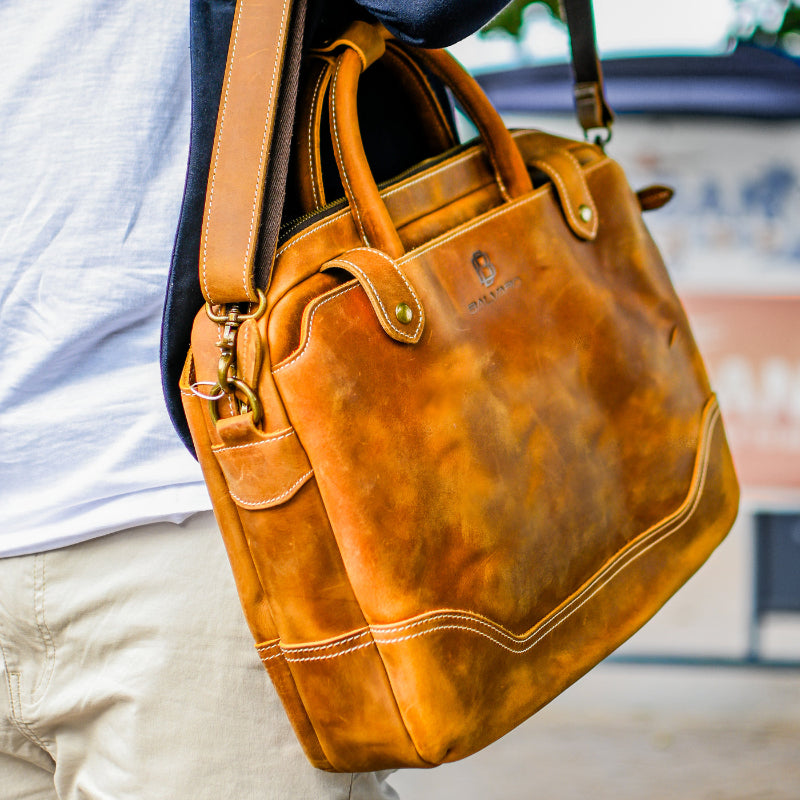 A person carrying a brown vintage leather laptop briefcase with a shoulder strap.